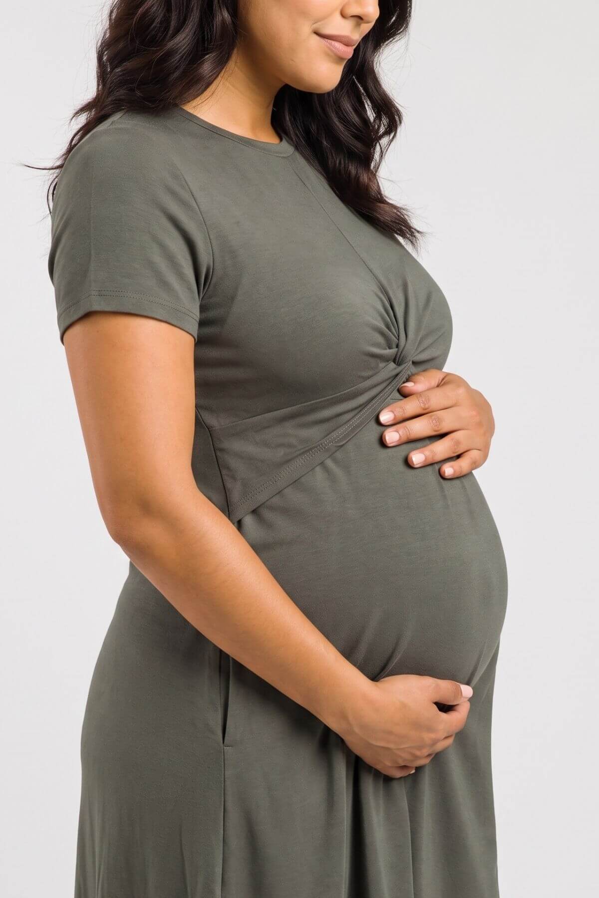 A pregnant woman wearing a short-sleeve olive green maternity dress, shown from the side against a light gray background.