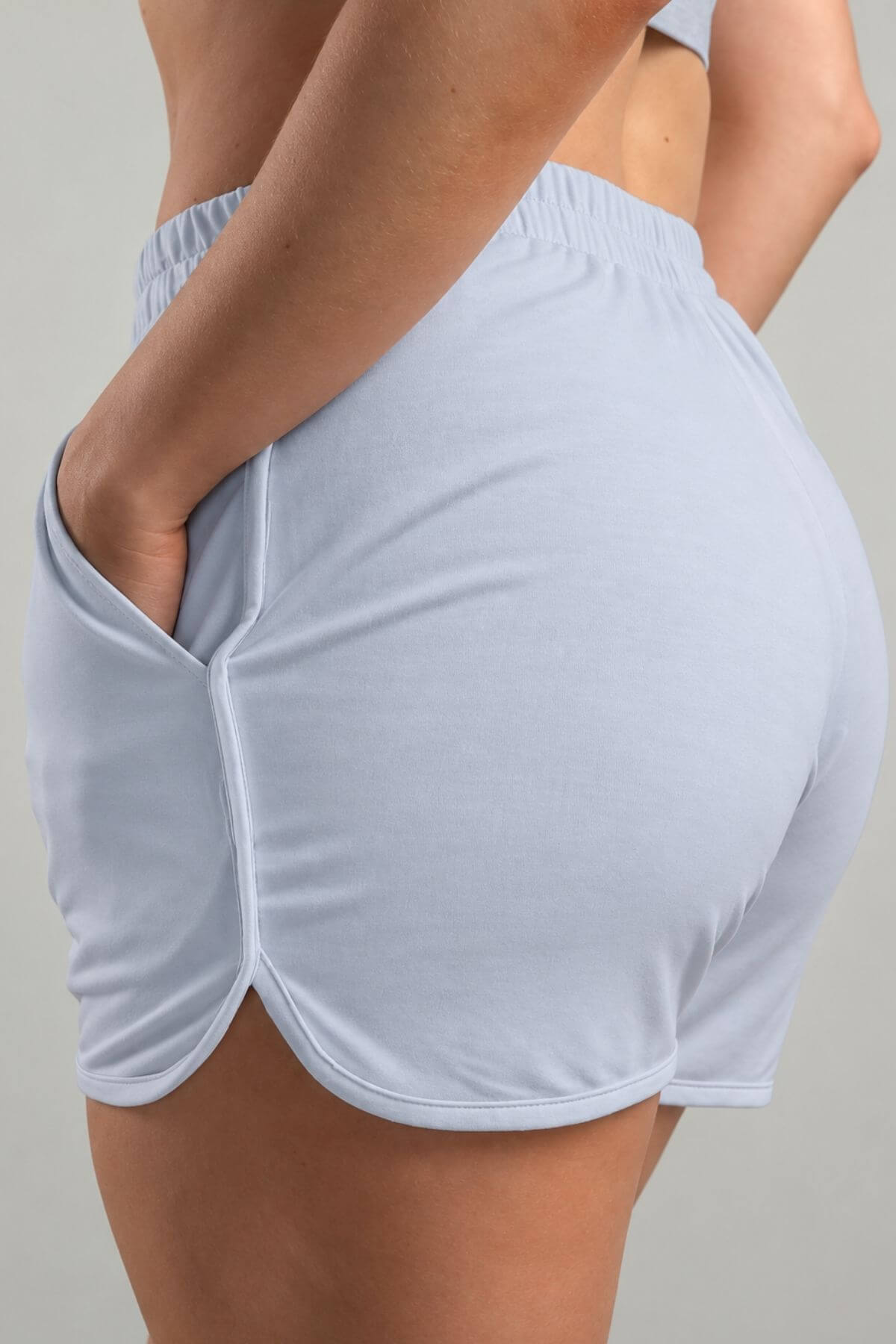 Close-up back view of a person wearing light blue athletic shorts with side pockets and an elastic waistband, shown against a plain light gray background.