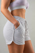 A close-up of a model wearing light heather gray drawstring shorts with side pockets, paired with a matching light lavender sports bra against a neutral gray background.