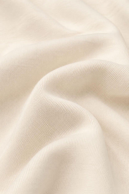 A close-up of draped cream-colored fabric with a fine ribbed texture and soft folds..