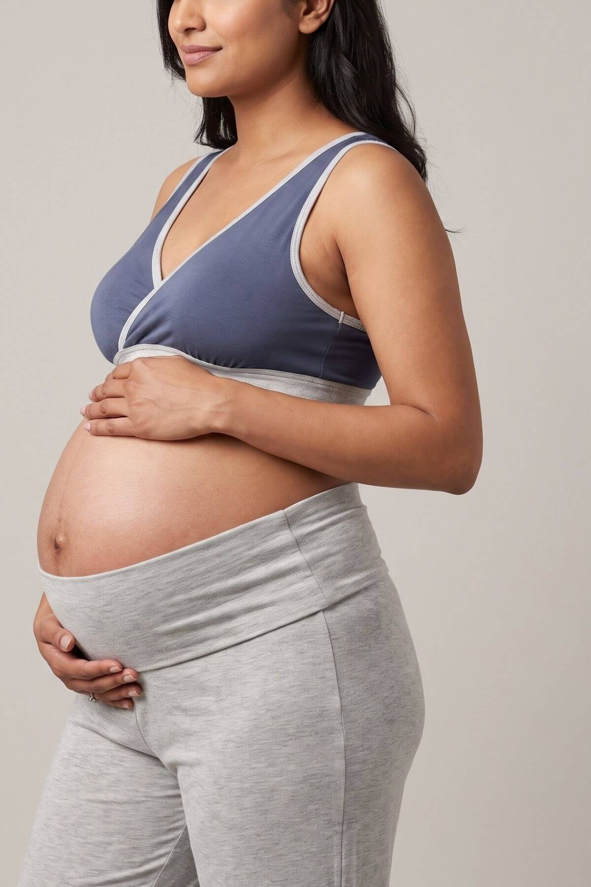 Pregnant woman wearing a slate blue and gray wrap-style maternity bralette with matching gray high-waisted leggings, shown from the side against a neutral studio background.
