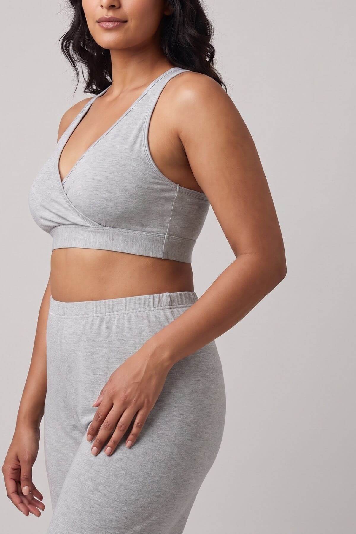 A woman wearing a light gray heathered sports bra and matching jogger pants against a solid light gray studio background.