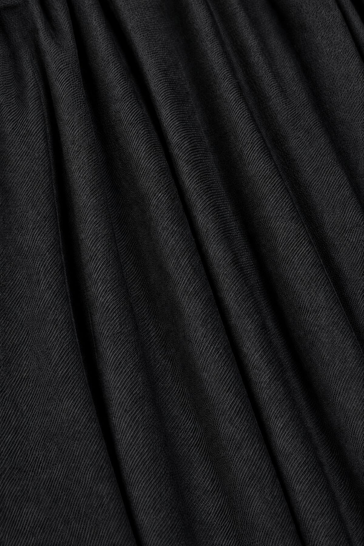 A close-up of black pleated fabric with a fine diagonal twill texture, showing soft vertical folds.