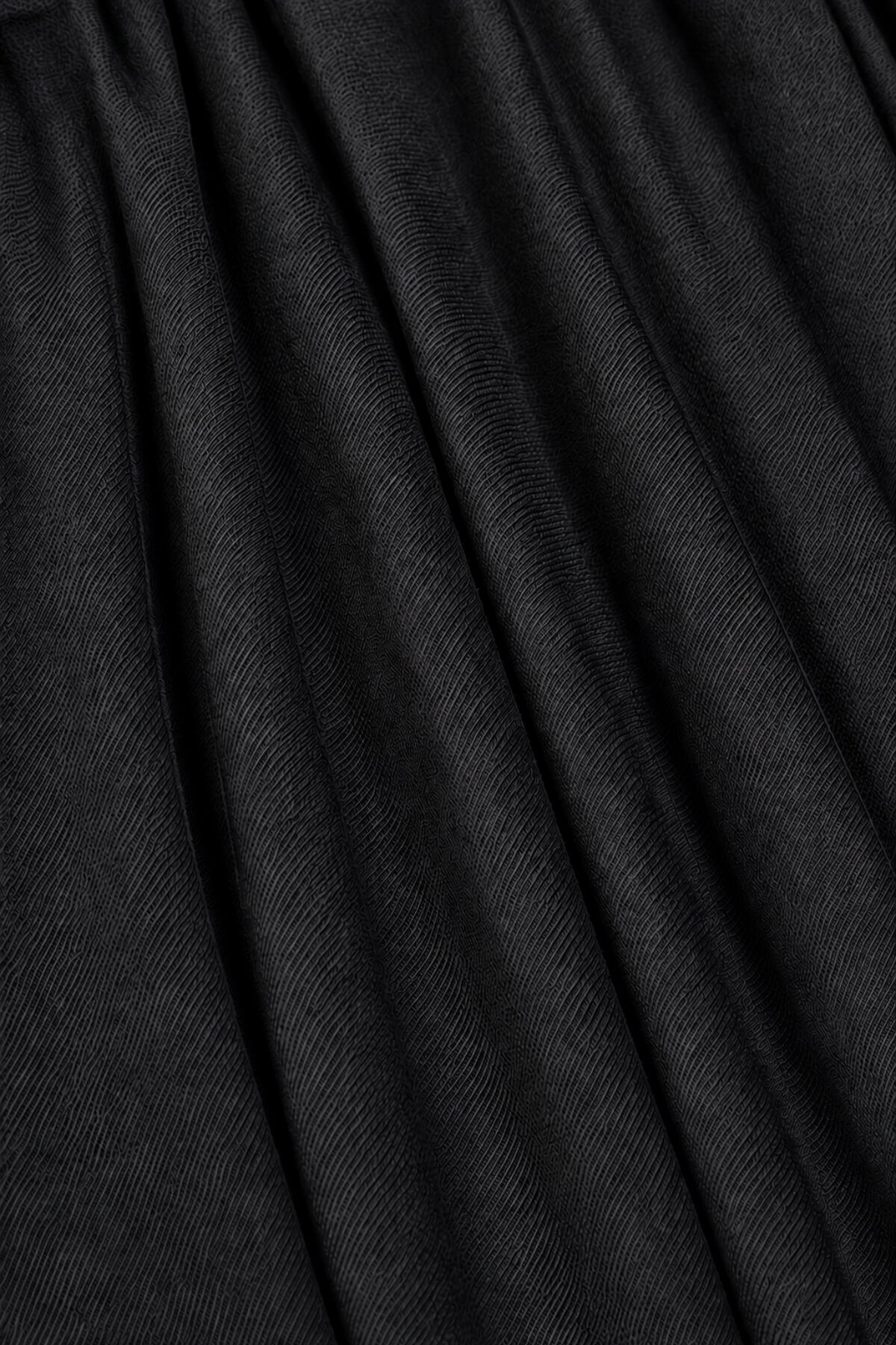 A close-up of black pleated fabric with soft vertical folds and a fine textured weave.