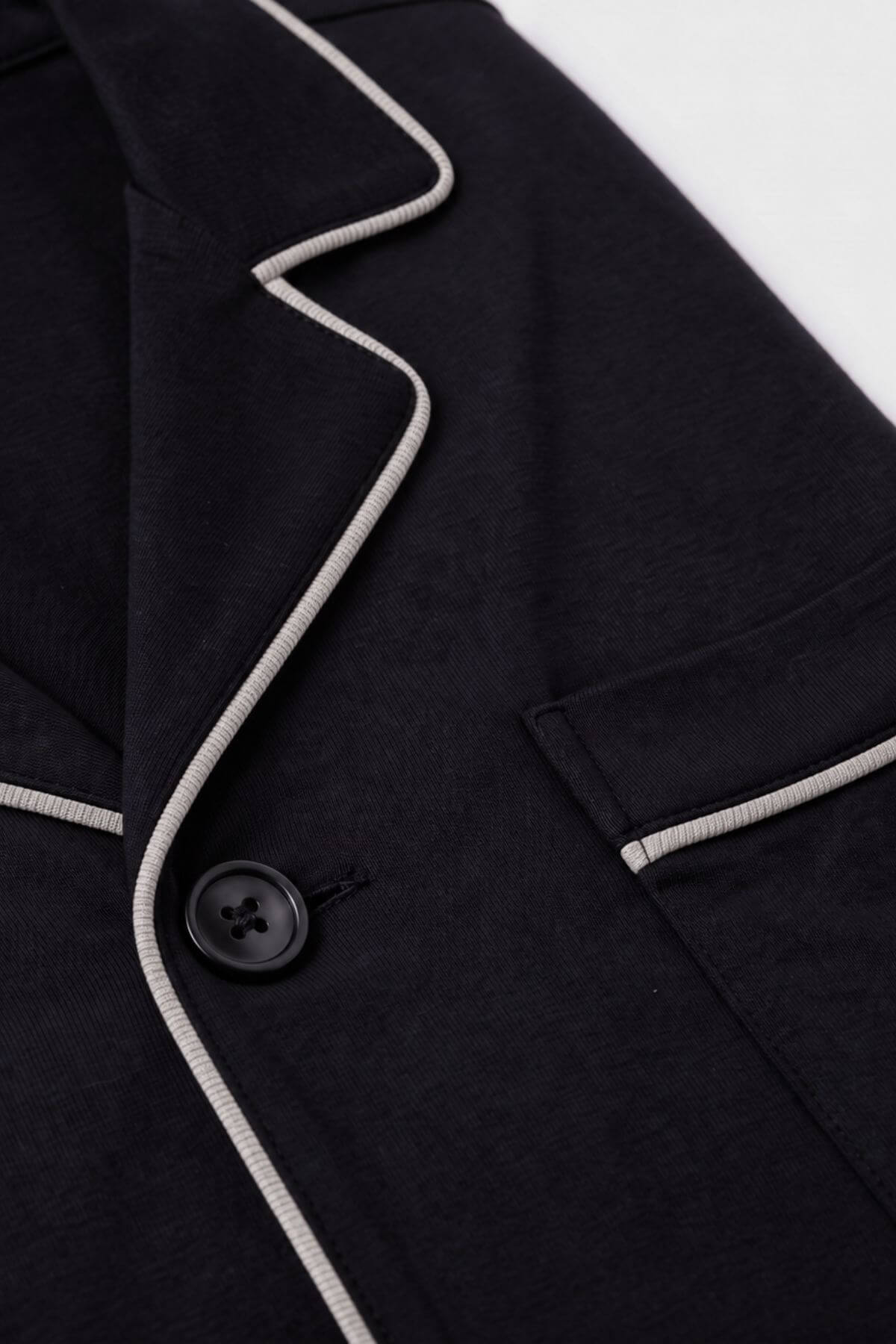 Close-up of a dark navy or black blazer with contrasting light gray piping along the lapel and pocket edges, featuring a black button.