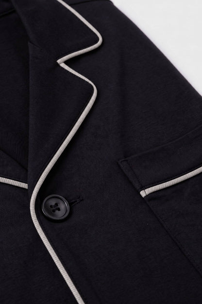 Close-up of a dark navy or black blazer with contrasting light gray piping along the lapel and pocket edges, featuring a black button.