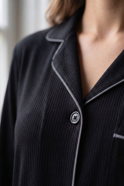 Close-up of a person wearing a dark ribbed pajama top with light piping and a button placket. 