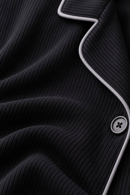 Close-up of a black ribbed knit garment, likely a cardigan or sweater, with contrasting light gray piping and a matching button.