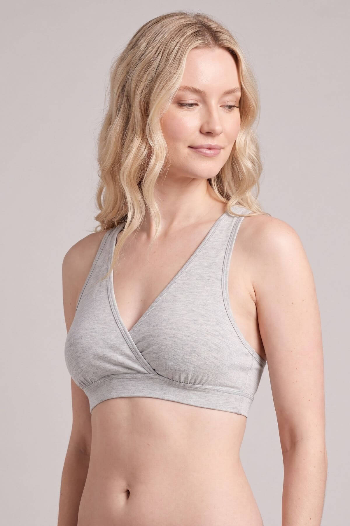 A blonde woman wearing a light gray heathered wrap-style bralette, shown from the chest up against a solid light gray studio background.