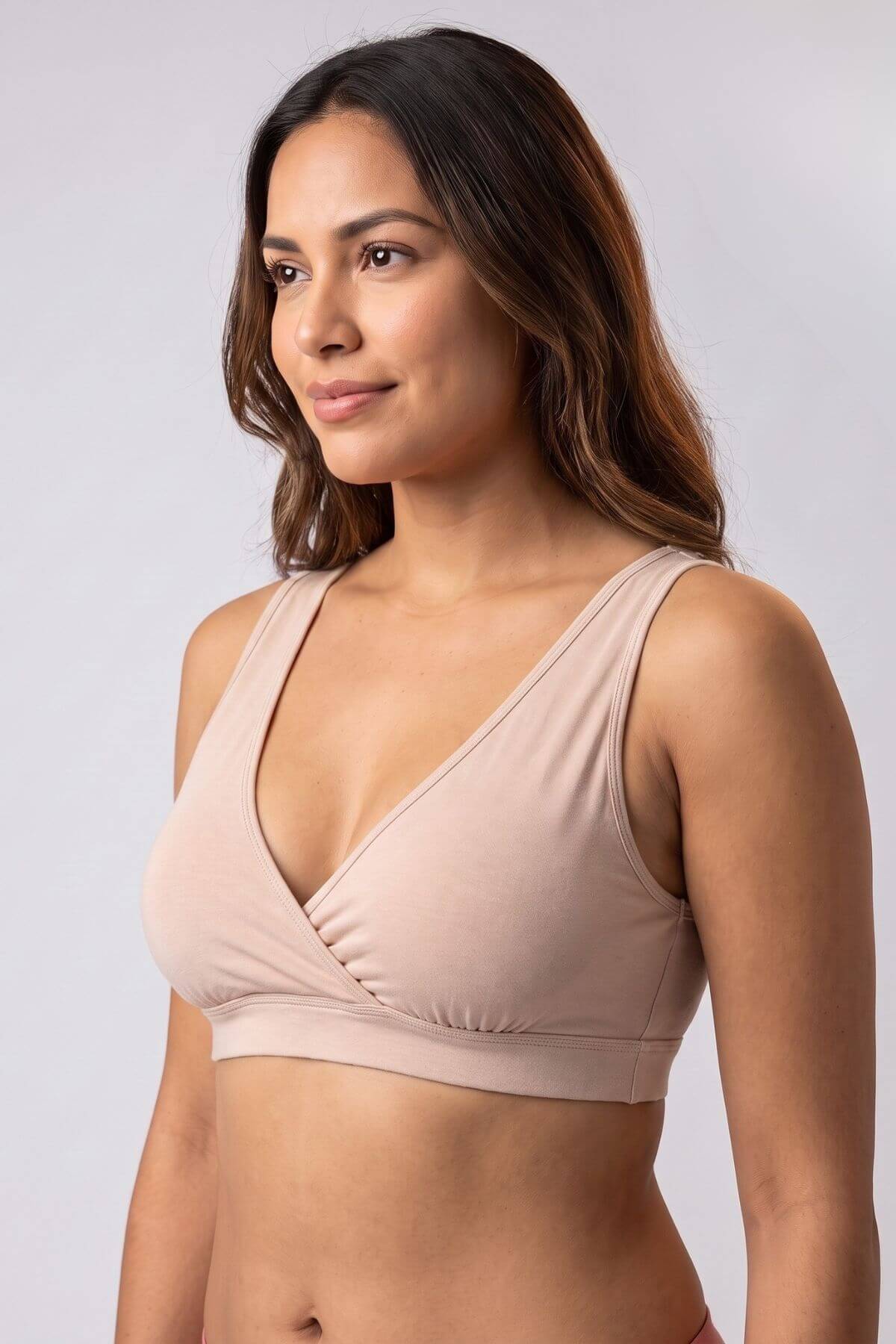 A woman modeling a light beige wrap-style bralette against a plain light gray studio background.