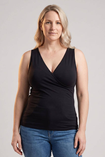 A woman modeling a black sleeveless wrap-style top with a deep V-neck, paired with blue jeans, against a plain light gray studio background.