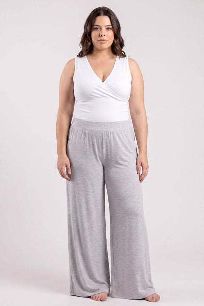A woman modeling a two-piece loungewear set consisting of a white wrap-style sleeveless top and light gray wide-leg sweatpants, photographed against a solid light gray studio background.