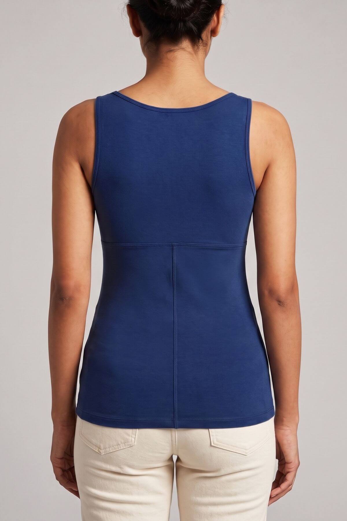 A woman viewed from the back wearing a sleeveless royal blue top and light beige pants against a plain light gray studio background.