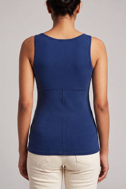 A woman viewed from the back wearing a sleeveless royal blue top and light beige pants against a plain light gray studio background.