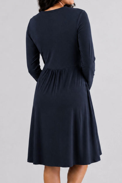 A woman wearing a dark navy long-sleeve midi dress, shown from the back against a light gray studio background