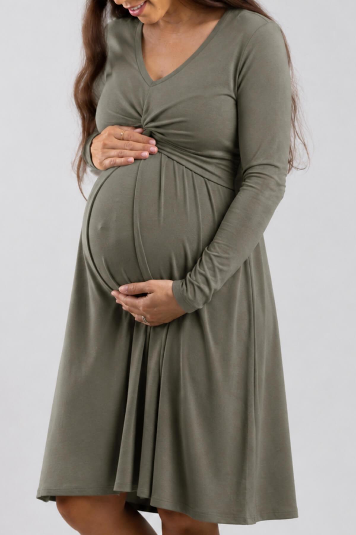 A pregnant woman wearing a long-sleeve olive green maternity dress with a gathered twist detail at the bust, shown against a plain light gray studio background