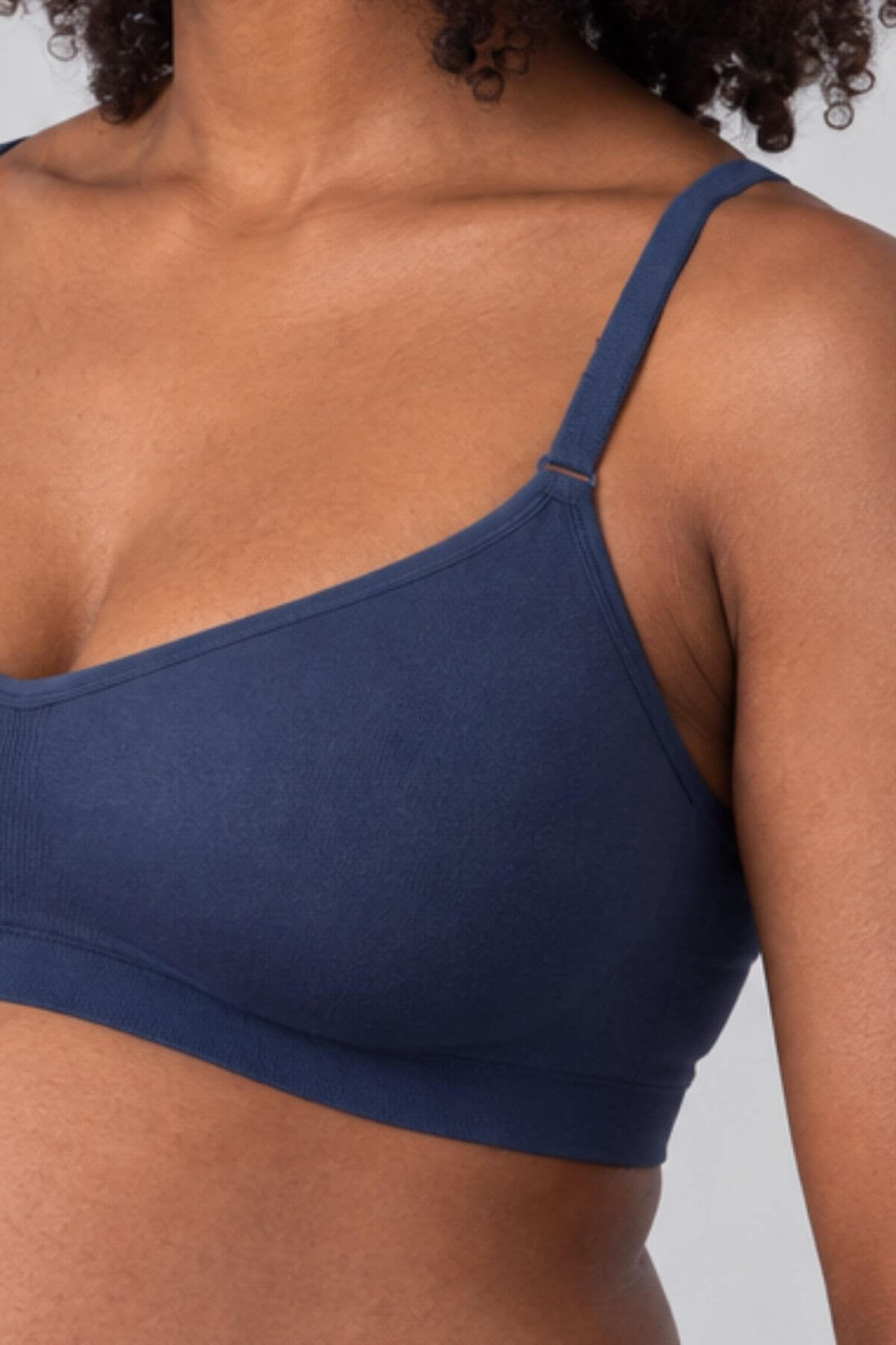 A close-up of a model wearing the Stages Nursing Bra, Maternity Bra, Wearable Pump Bra and Everyday Bra all-in-one in indigo against a light gray background.