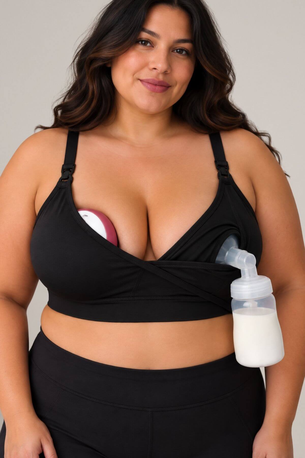 A plus size woman wearing simple wishes supermom silhouette nursing and hands free pumping bra, shown with a breast pump attached to the side and an in bra wearable breast pump supported in the other cup, against a plain light gray background.