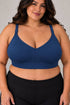 A woman wearing the supermom silhouette nursing and hands free pumping bra and black high-waisted leggings, shown from the chest down against a plain light gray studio background.