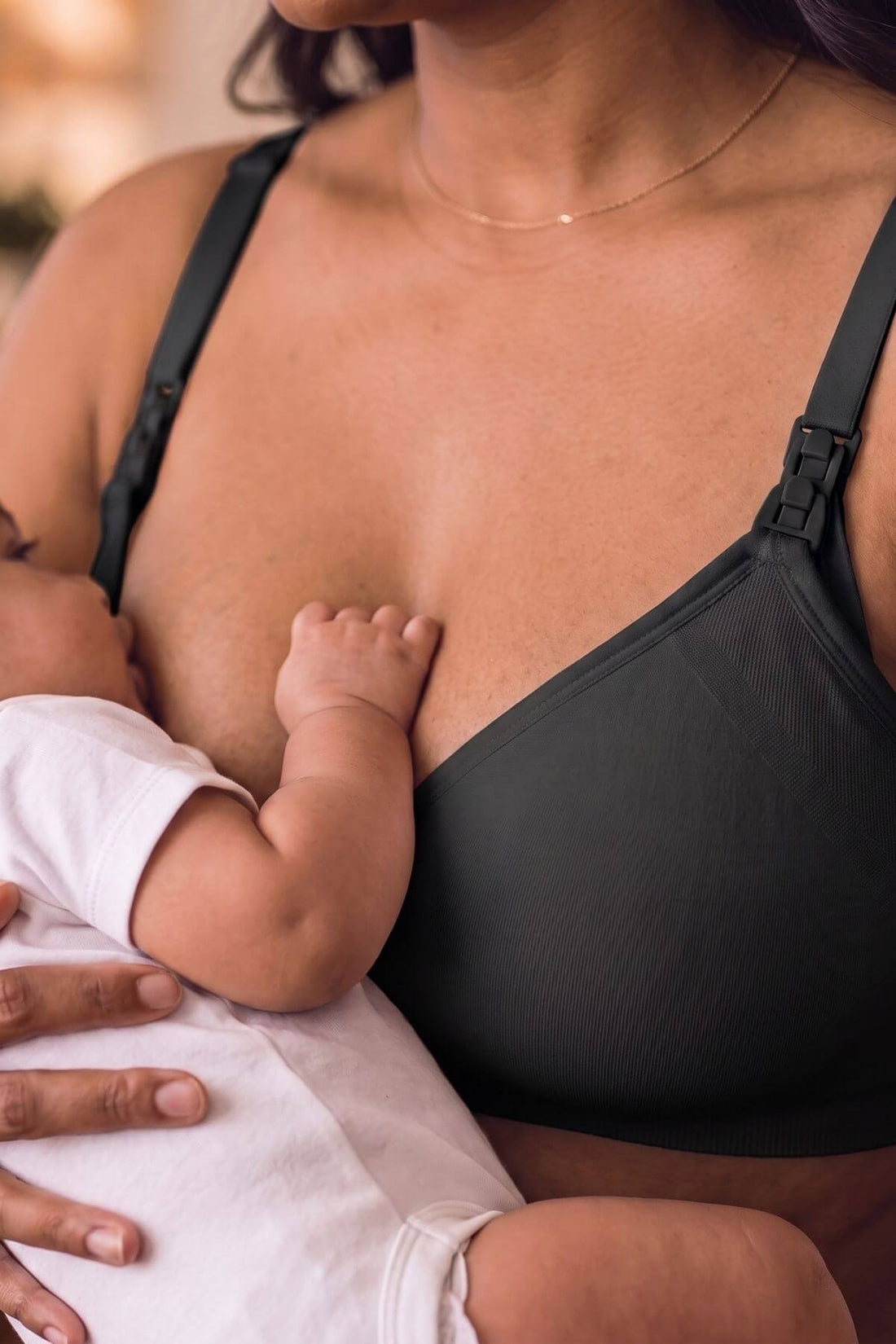 A close-up lifestyle shot of a woman breastfeeding a baby, wearing the  simple wishes silhouette nursing &amp; hands free pumping bra.