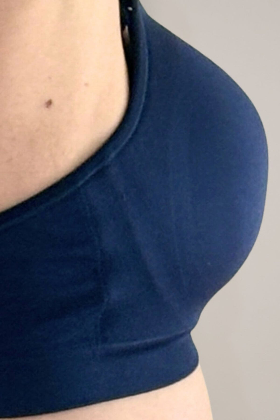 Close-up of a person wearing the supermom silhouette nursing &amp; hands free pumping bra in indigo, showing the side profile and underwire area against a plain light gray background.