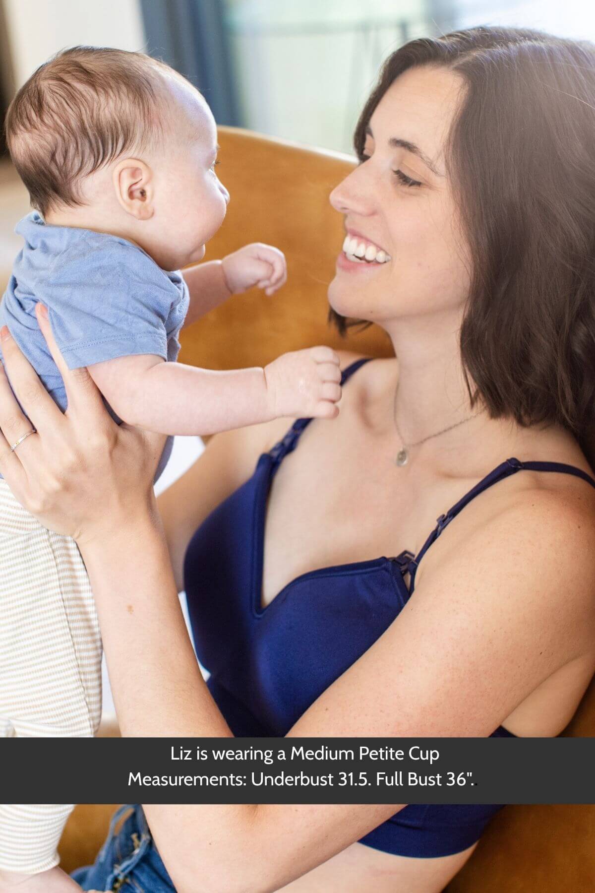 A woman holding a baby while wearing a the supermom silhouette nursing and hands free pumping bra in indigo. A text banner at the bottom provides sizing information: &