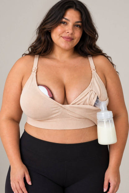 A woman wearing the supermom silhouette nursing and hands free pumping bra shown with a breast pump bottle connected to one cup and in in bra wearable pump supported in the other. She is also wearing black leggings against a plain light gray studio background.