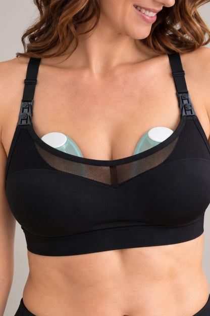 A close-up of a woman wearing the supermom sweetheart mesh racerback nursing &amp; hands-free pumping sports brawith a sheer mesh V-neck panel and front adjust shoulder straps. Two Elvie Stride in bra wearable pumps are placed under the bra cups.